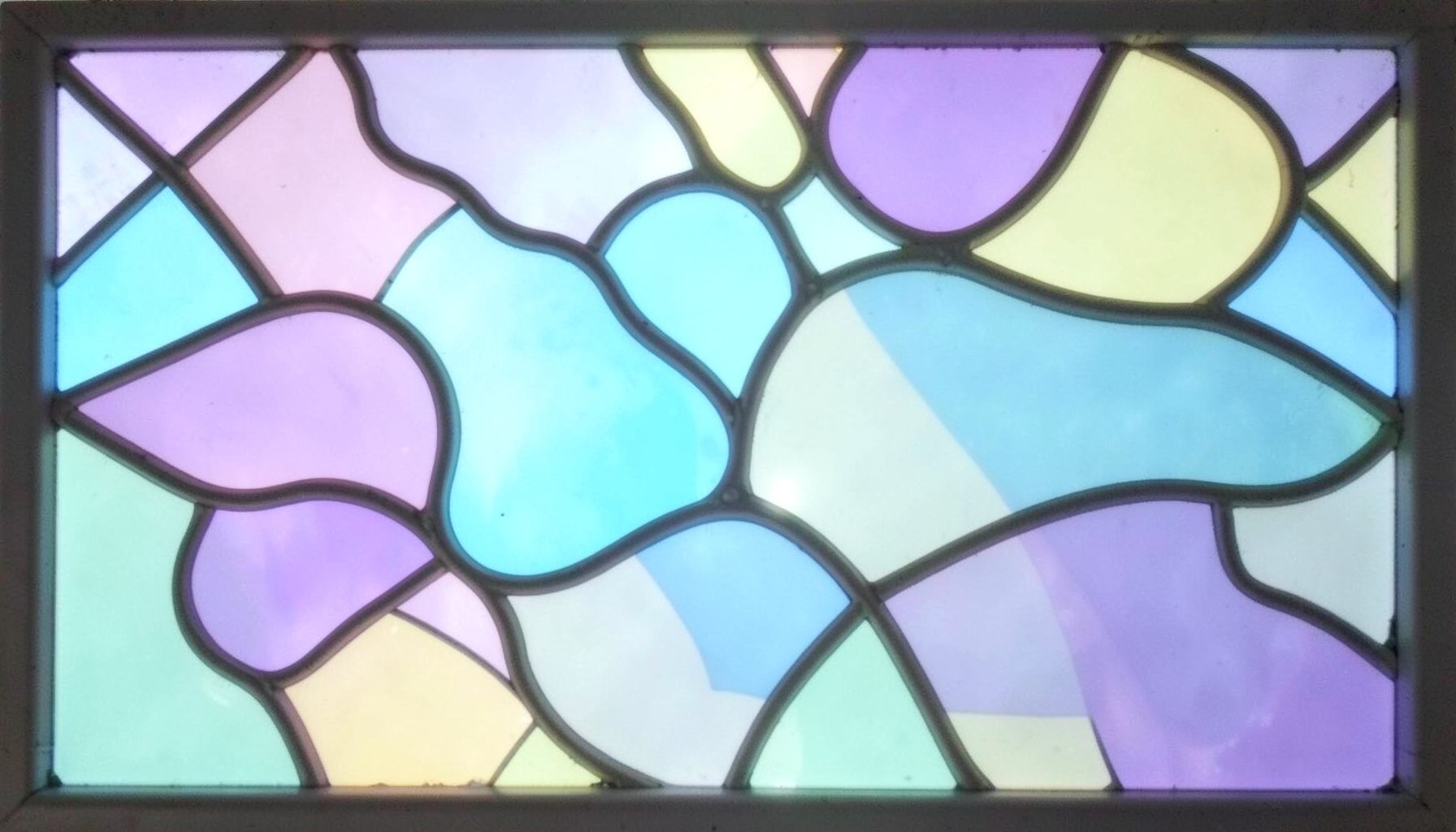 A stained-glass composition in soft pastel lavender, mint, and pale yellow with rounded leaded shapes suggesting playful, childlike wonder.