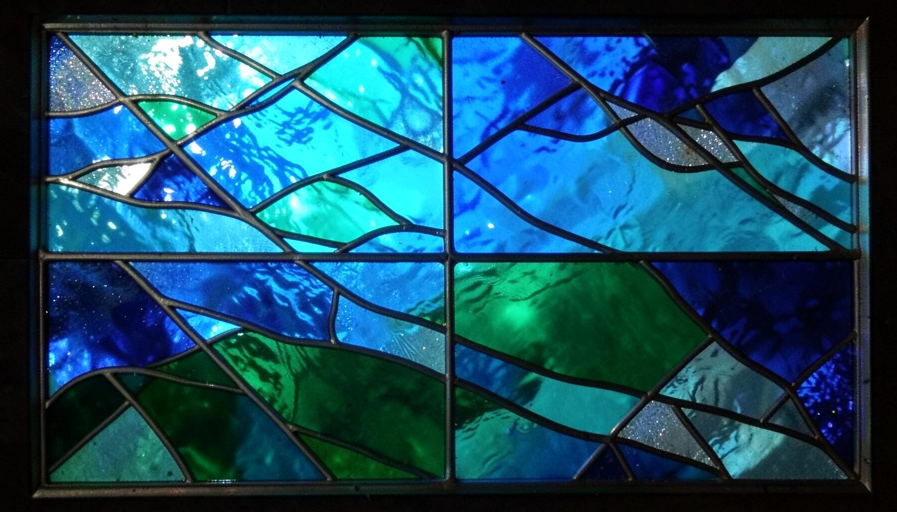 A stained-glass panel in oceanic blues and greens with shimmering silver segments, evoking underwater light and mermaid-inspired whimsy.