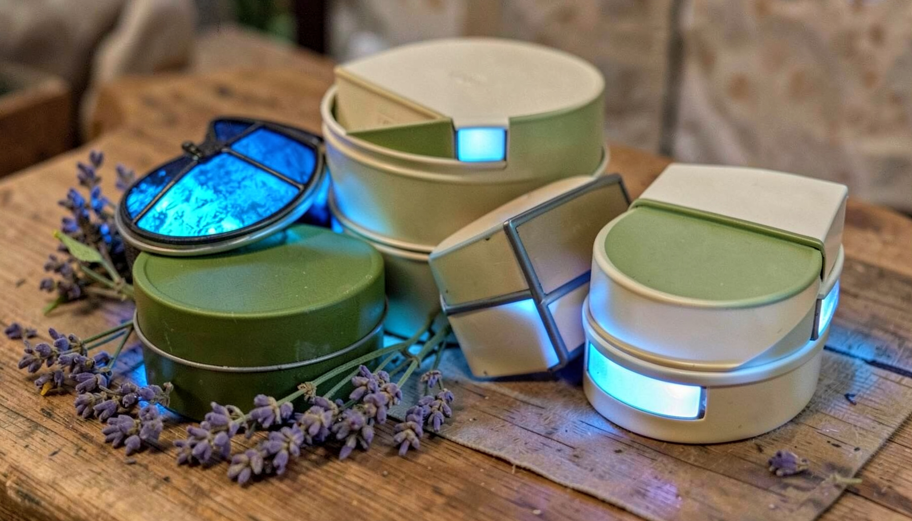 An assortment of natural skincare tins and tubes in earthy green and cream packaging, arranged on a wooden surface with a sprig of lavender.