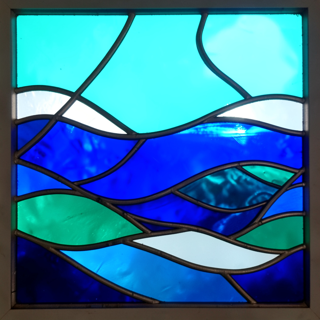 A stained-glass style ocean scene with turquoise, cobalt, and white leaded glass segments suggesting waves and a playful underwater mood